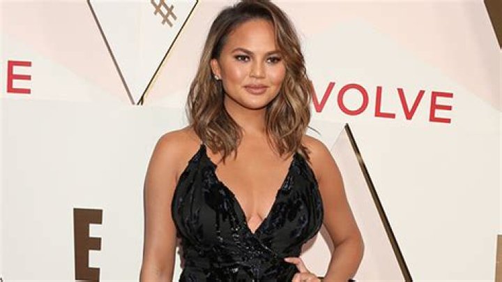 Chrissy Teigen Rocks Bike Shorts, High Boots & ‘Michelle Obama’-Inspired Gold Belt For Dress Up Look